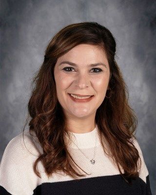 Woman with brown hair, smiling, wearing a sweater, against a mottled gray background.