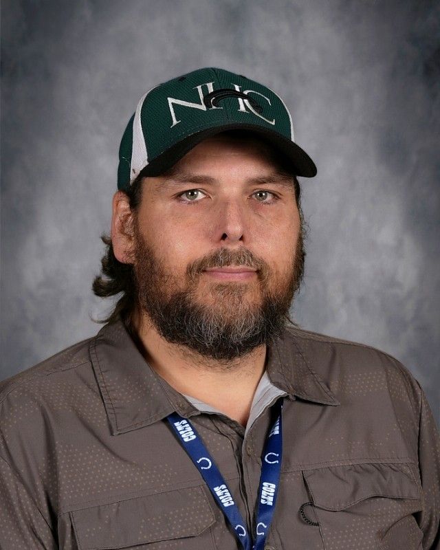 Man wearing a green cap, light blue shirt, and a salt and pepper beard looking at the viewer.
