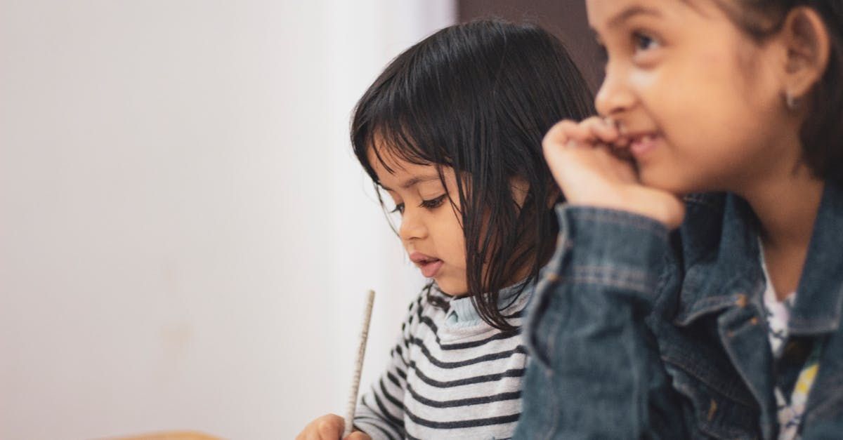 Two young girls drawing, one in striped shirt, the other smiling in a denim jacket.