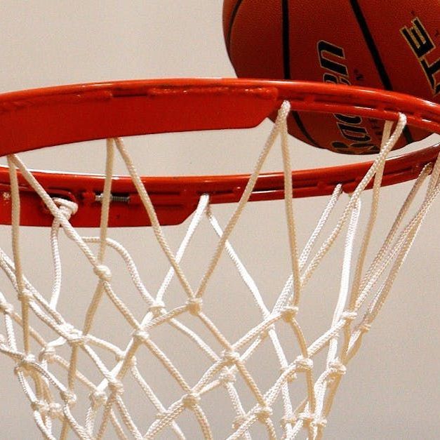 Basketball partially in the hoop, orange rim, white net, light background.