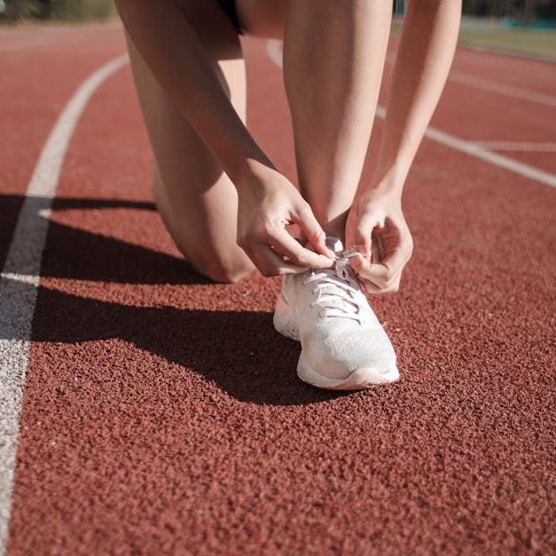 Runner on track, tying shoelace of white sneaker. Close up.