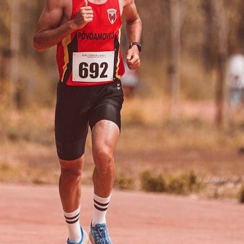 Runner wearing bib number 692 in red and black uniform, running on a track.