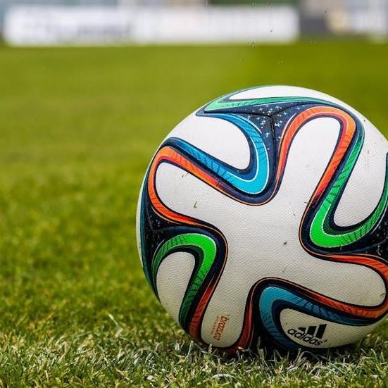Soccer ball on green grass field, with blue, orange, green, and black accents, Adidas logo visible.