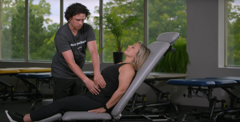 A man is helping a pregnant woman stretch her legs on a couch.