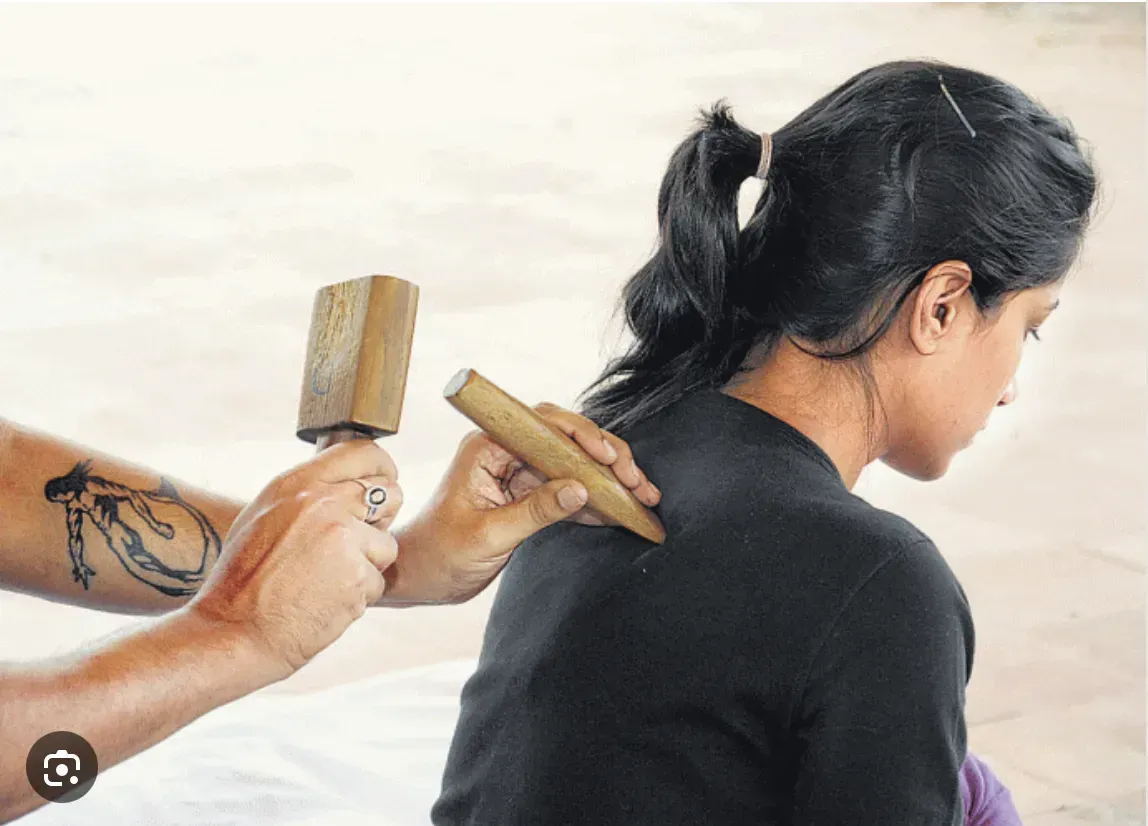 A woman is getting a massage with a wooden stick on her back.