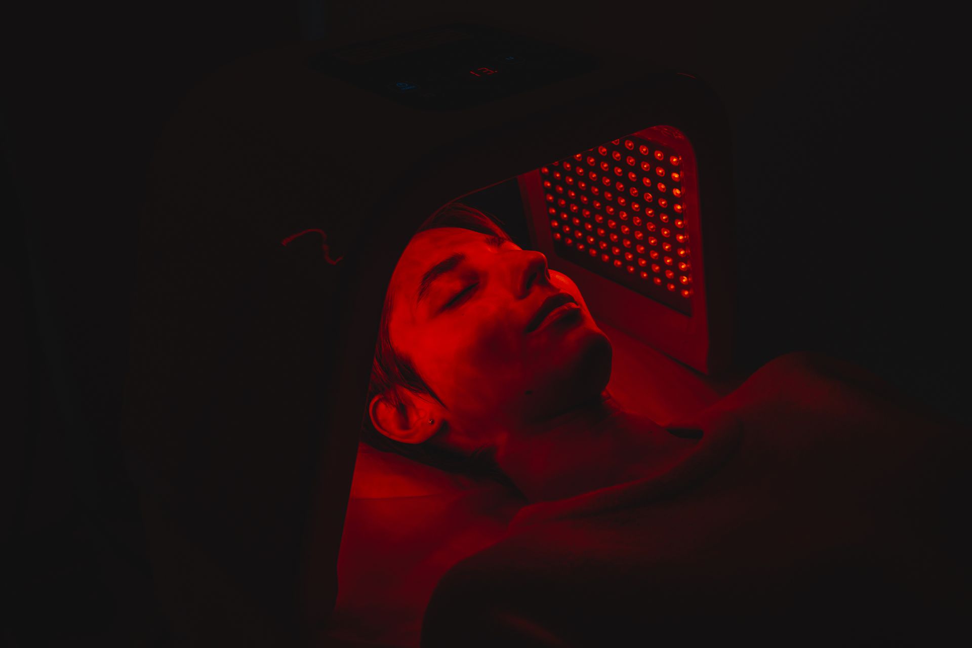 Person receiving red light therapy. Face illuminated in red light, eyes closed.