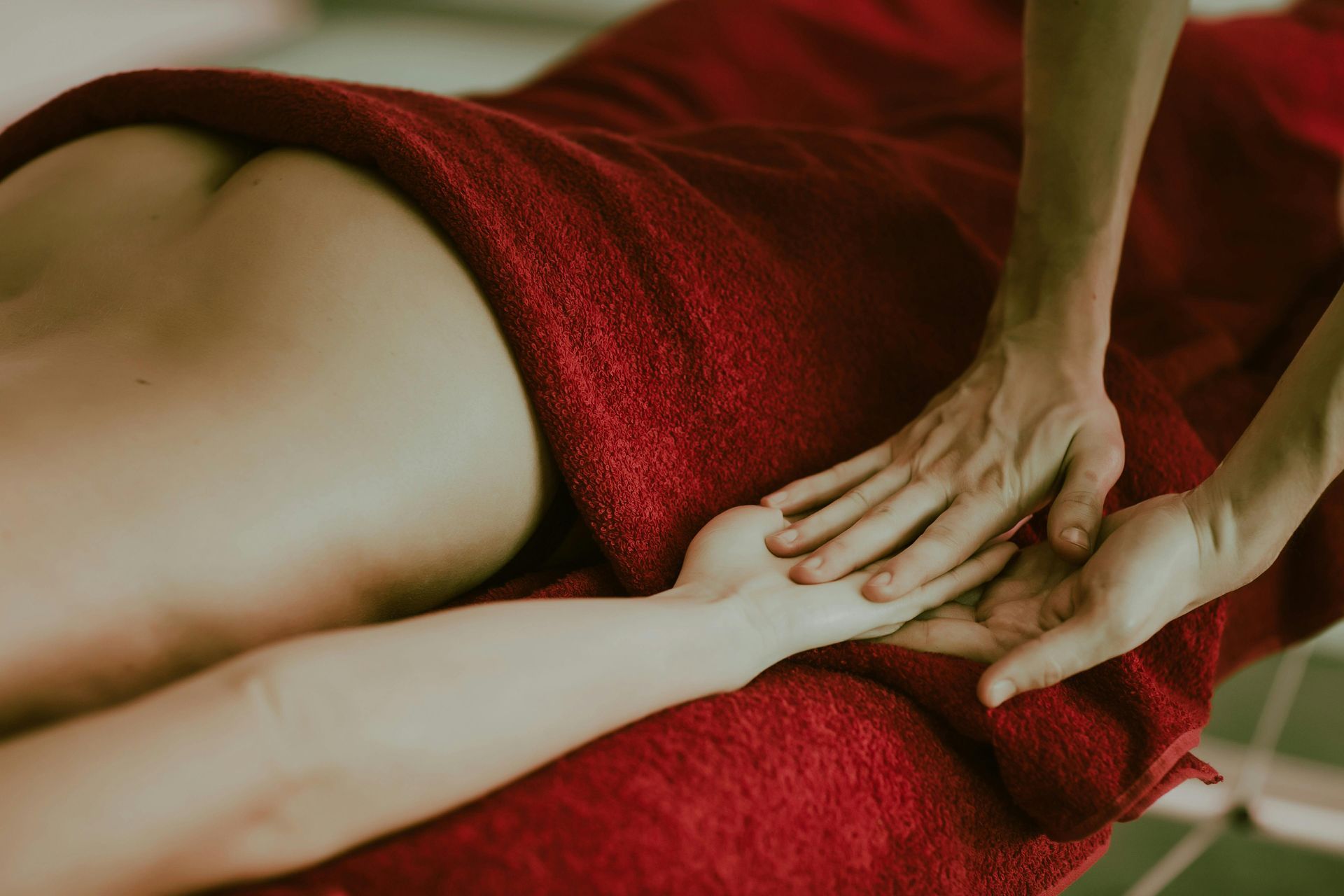 Hands massaging a forearm on a red towel-covered surface; spa setting.