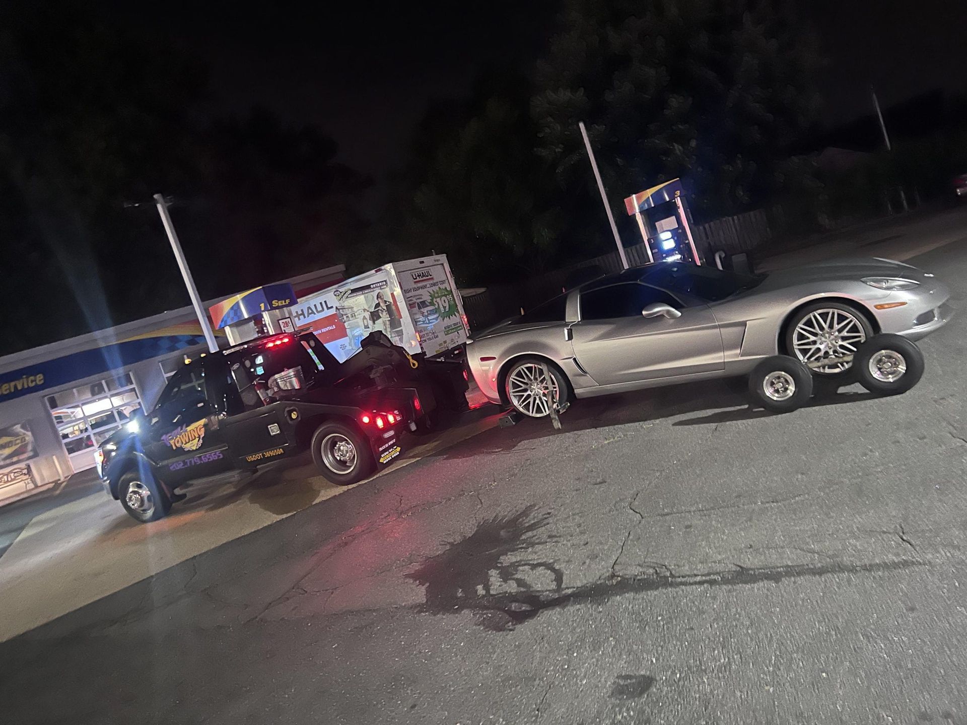 A car is being towed by a tow truck at night.