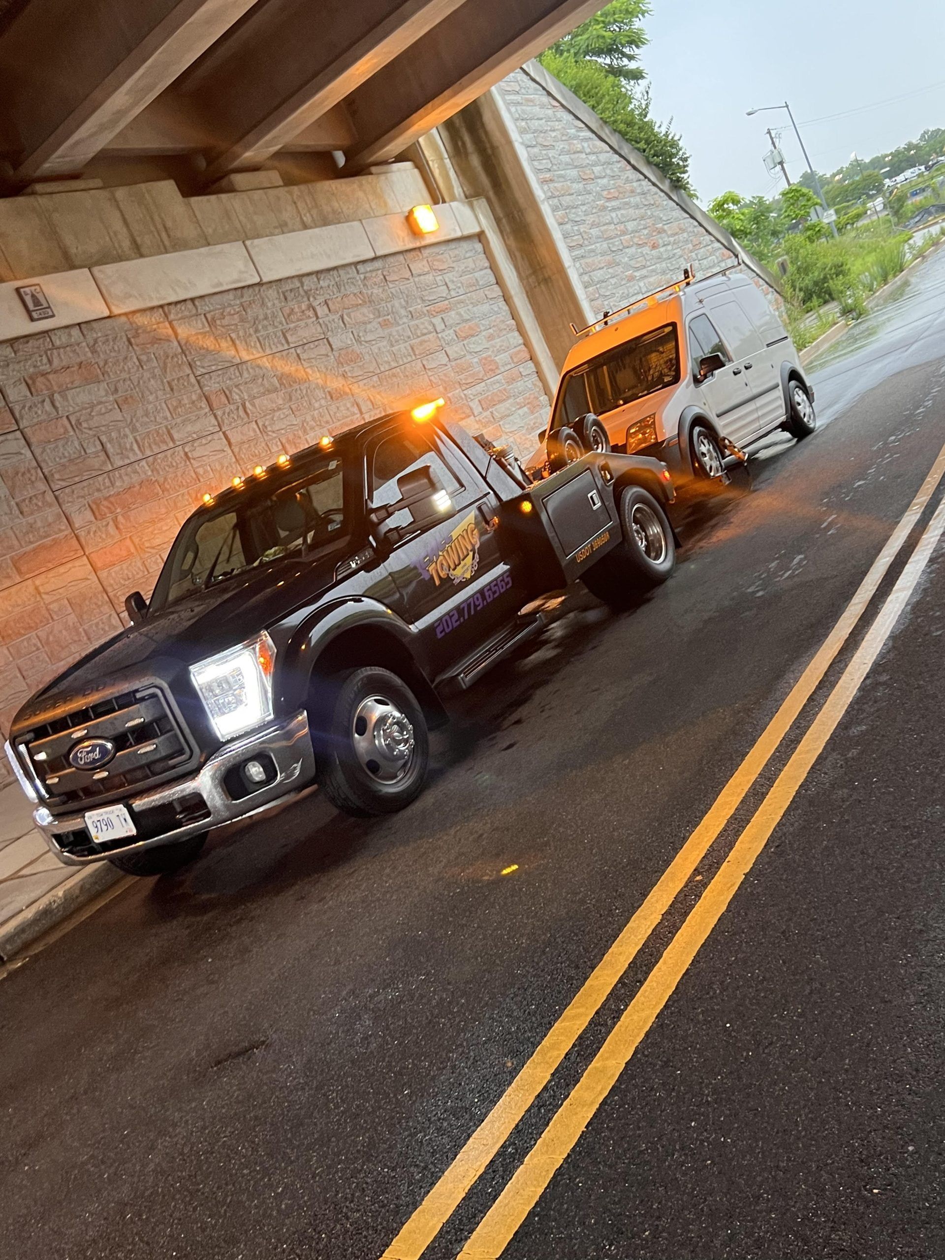 A tow truck is parked on the side of the road under a bridge.