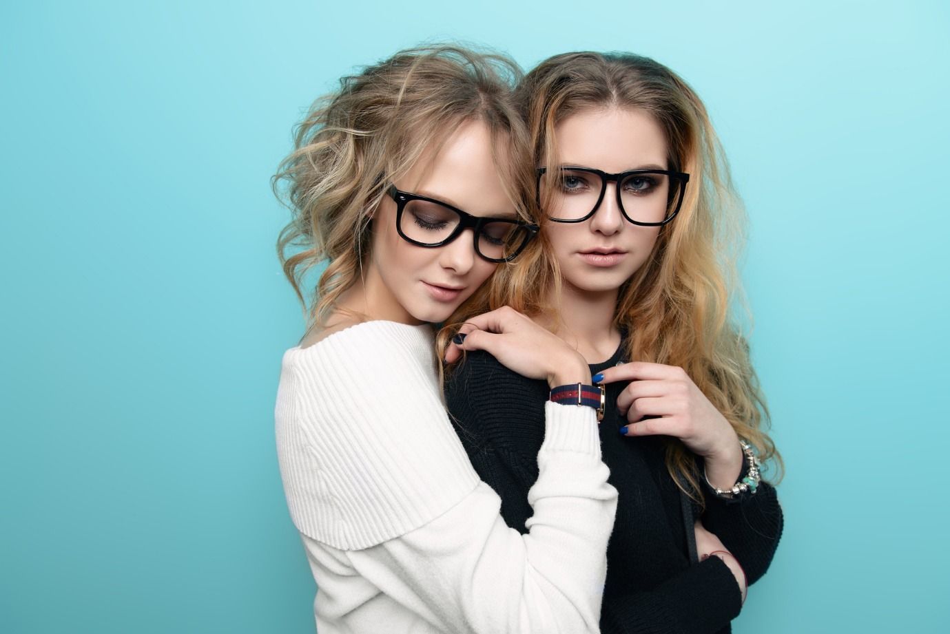 Dos mujeres que llevan gafas se abrazan sobre un fondo azul.