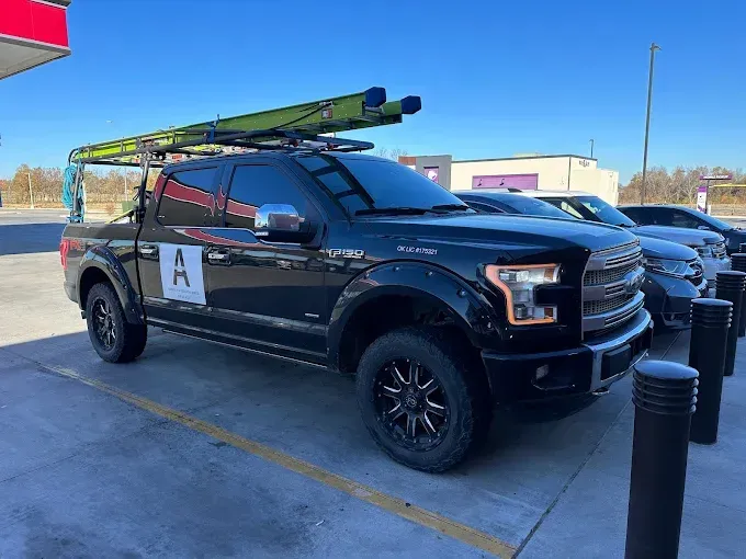 Black Ford pickup truck with ladder rack, parked at a gas station.