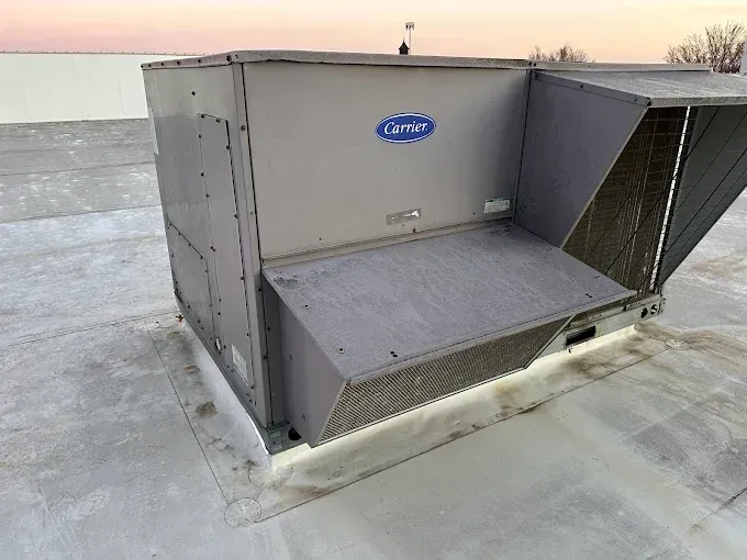 Carrier rooftop HVAC unit on a gray, flat roof. Gray and blue with vent and panel.