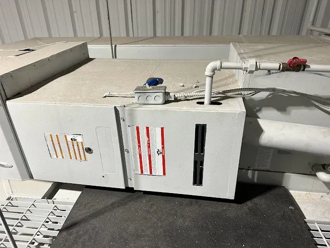 HVAC unit with a red and white sticker, pipes, and vents in a commercial setting.