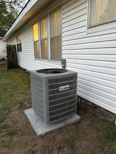 Gray air conditioner unit next to a white house on a concrete pad.
