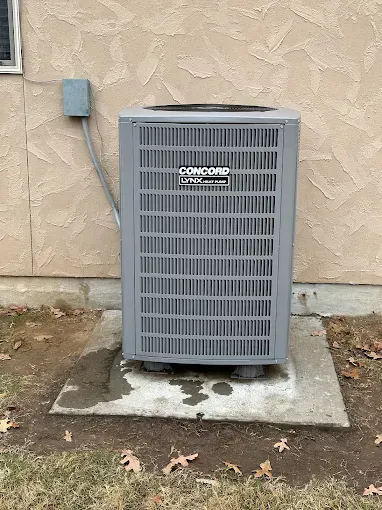 Gray air conditioning unit on a concrete pad next to a beige building.