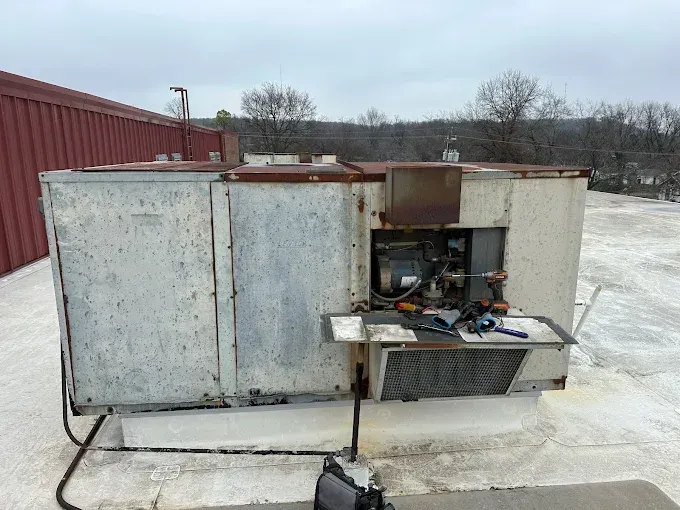 HVAC unit on a rooftop being worked on. Gray metal, tools visible. Cloudy day.