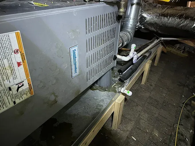 A furnace unit with water leakage. It is placed on wooden supports in an attic space.