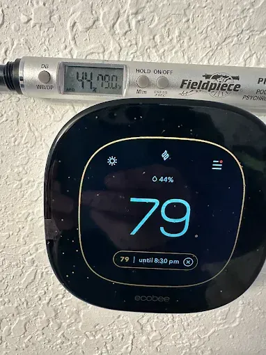 Thermostat showing 79 degrees, Fieldpiece meter displaying 44.000, mounted on a textured white wall.