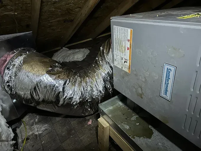 HVAC unit and ductwork in an attic with water damage and stains.