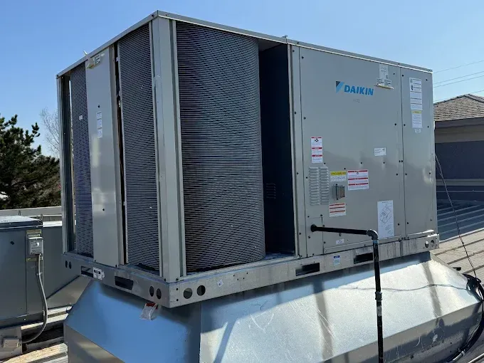 Daikin rooftop HVAC unit on a building, gray metal with black piping, sunny outdoor setting.