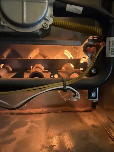 Furnace with lit burners, seen through a metal frame. Orange flames glow in the dark interior.