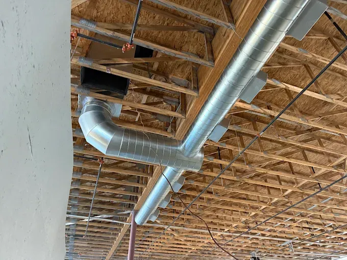 Galvanized metal HVAC ductwork installed in a building under construction, attached to wooden ceiling joists.