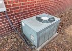An outdoor air conditioning unit on a concrete pad next to a brick wall.