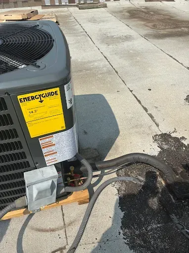 AC unit on a rooftop, next to black tar stains and lines, with a yellow energy guide label.