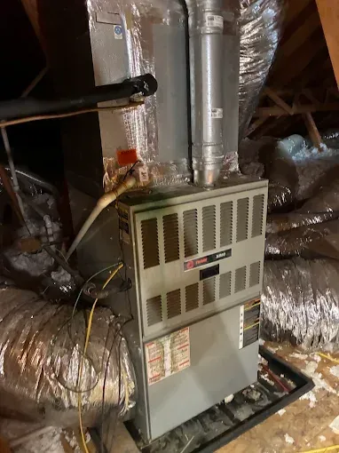 A Trane HVAC unit installed in an attic. Metal cabinet with ductwork and pipes.