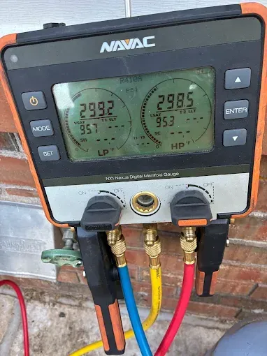 HVAC digital manifold gauge displaying pressure readings with hoses attached outside.
