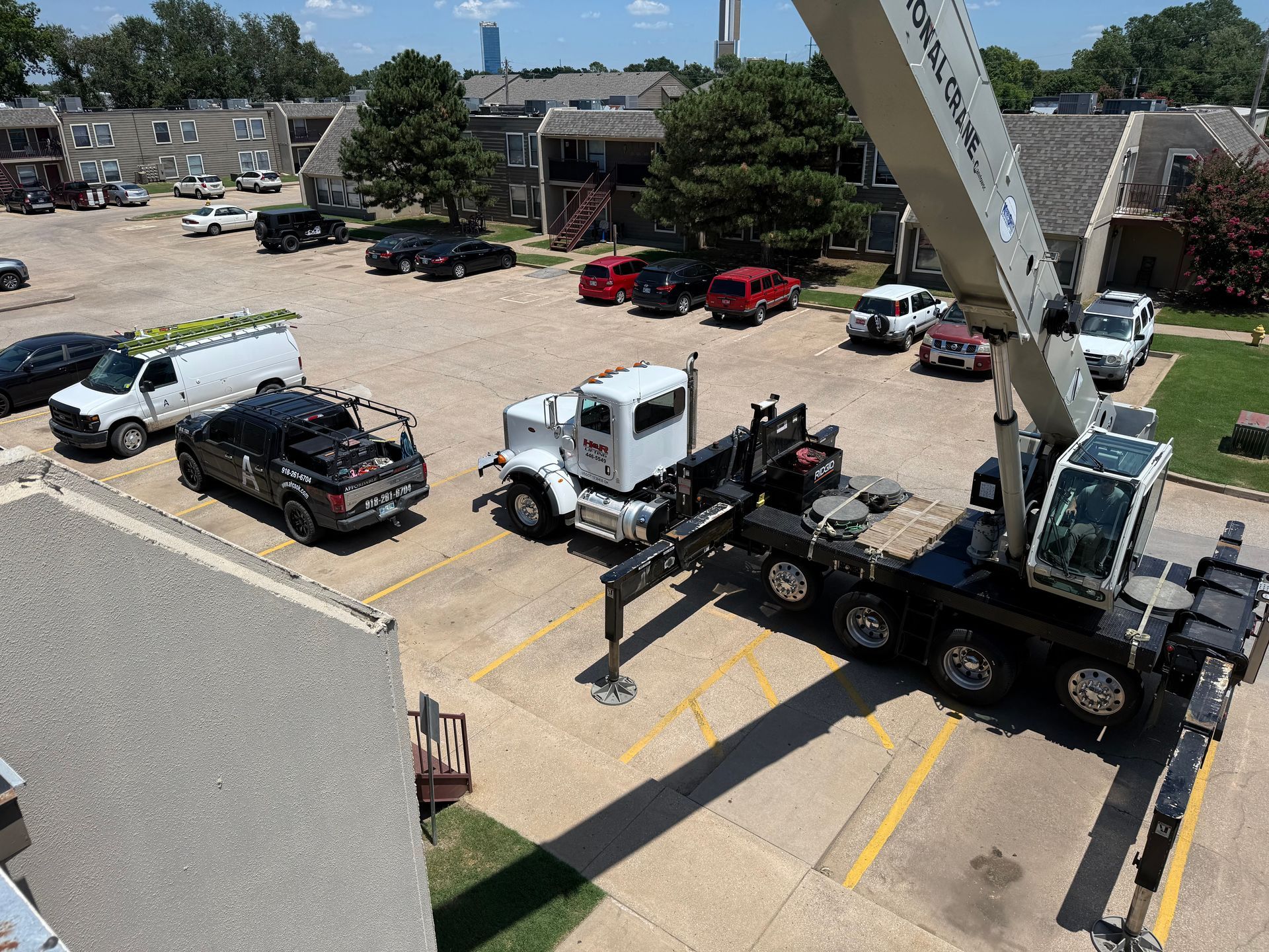 A crane lifting equipment at an apartment complex, with several vehicles parked nearby.