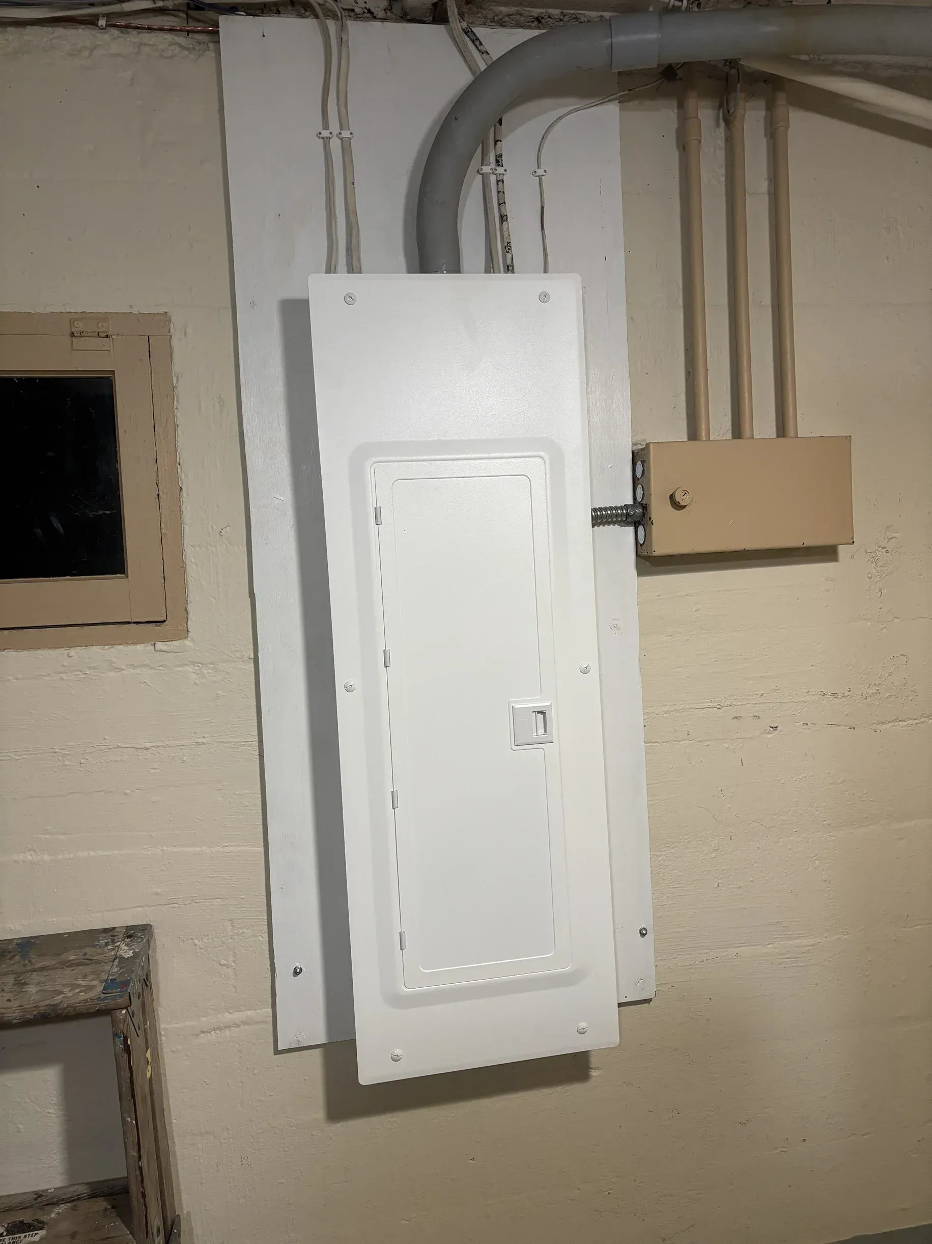 A white electrical box is hanging on a wall in a basement.
