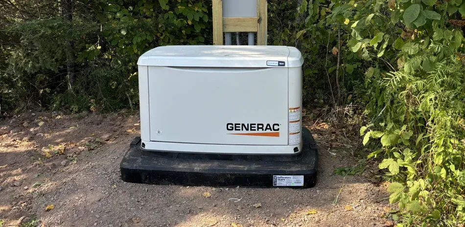 A generator is sitting on top of a black pallet in the middle of a forest.