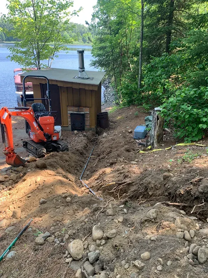 A small excavator is digging a hole in the dirt near a lake.