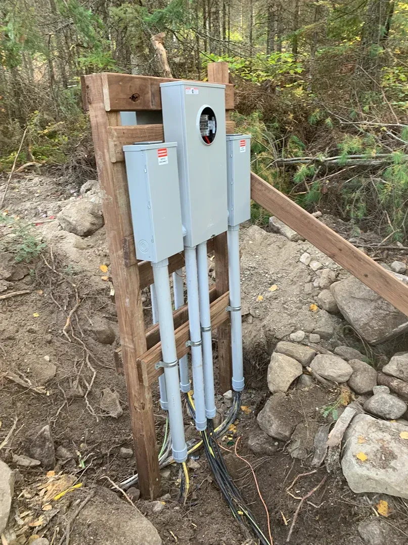A electrical box is sitting on top of a wooden post in the woods.