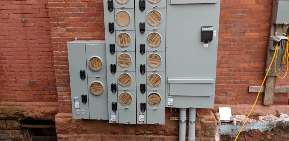 A large electrical box is sitting on the side of a brick building.