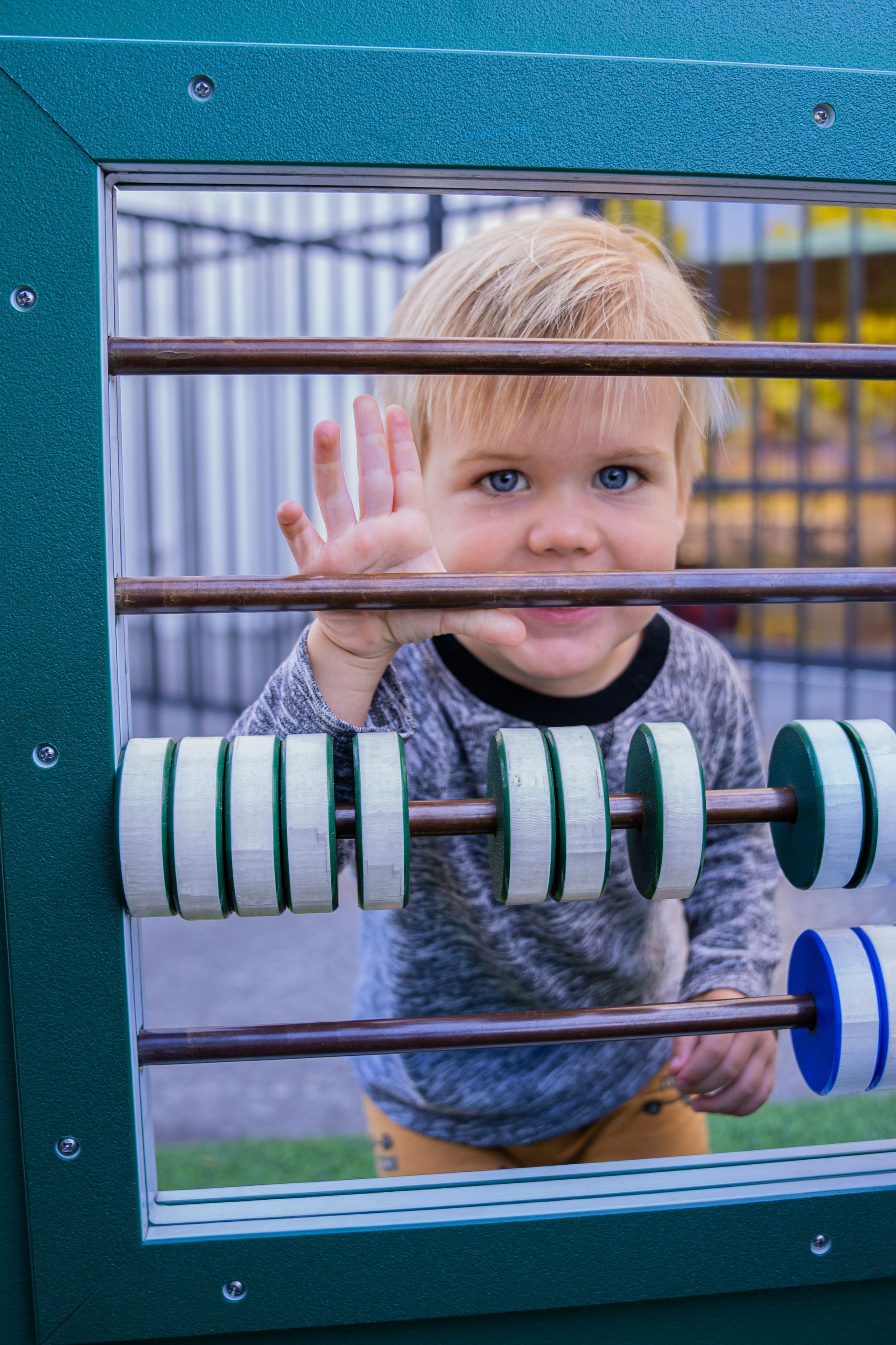 Young child with blonde hair, blue eyes, and a gray shirt plays with an abacus outdoors.