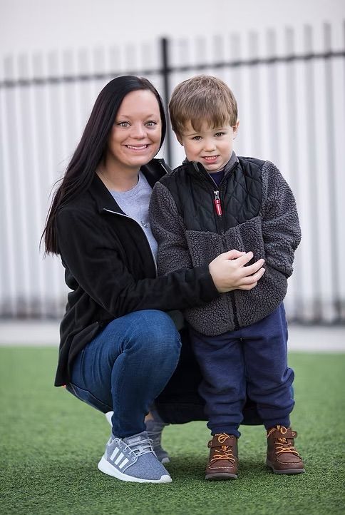 Woman and child posing together on green turf; the woman smiles while kneeling, child smiles standing.