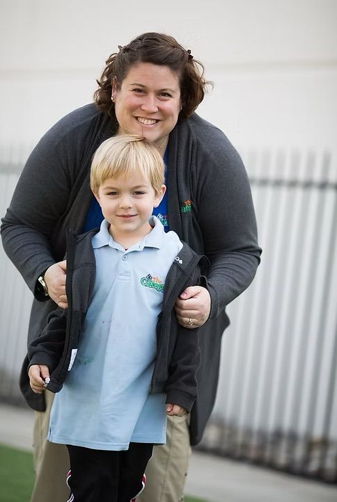Woman and young boy smiling at the camera, outside. Woman has arms around boy.
