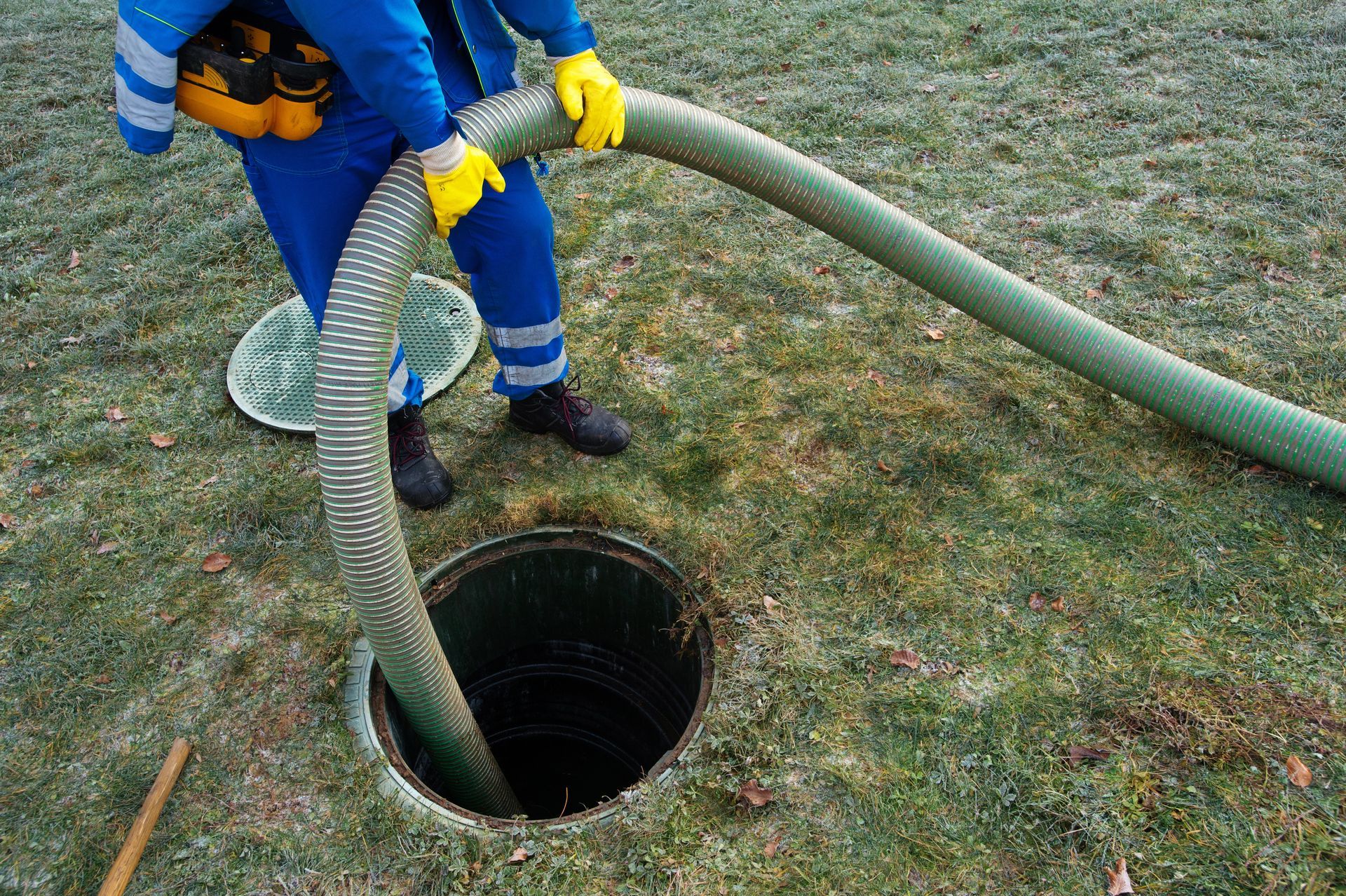 Worker emptying and cleaning a household septic tank to remove sludge and maintain the septic system.