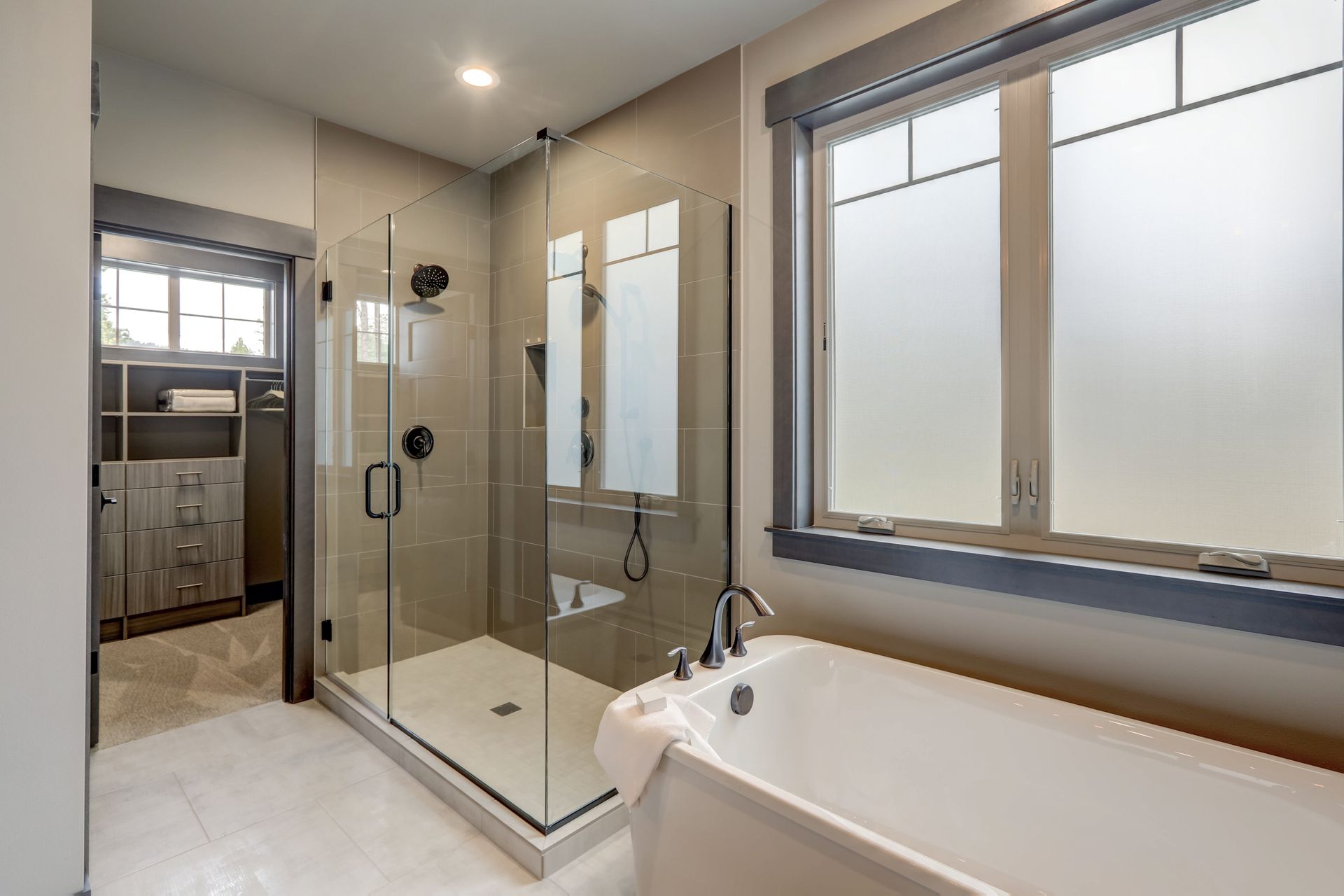 Modern bathroom interior with a glass walk-in shower, a white bathtub, and a spacious walk-in closet.