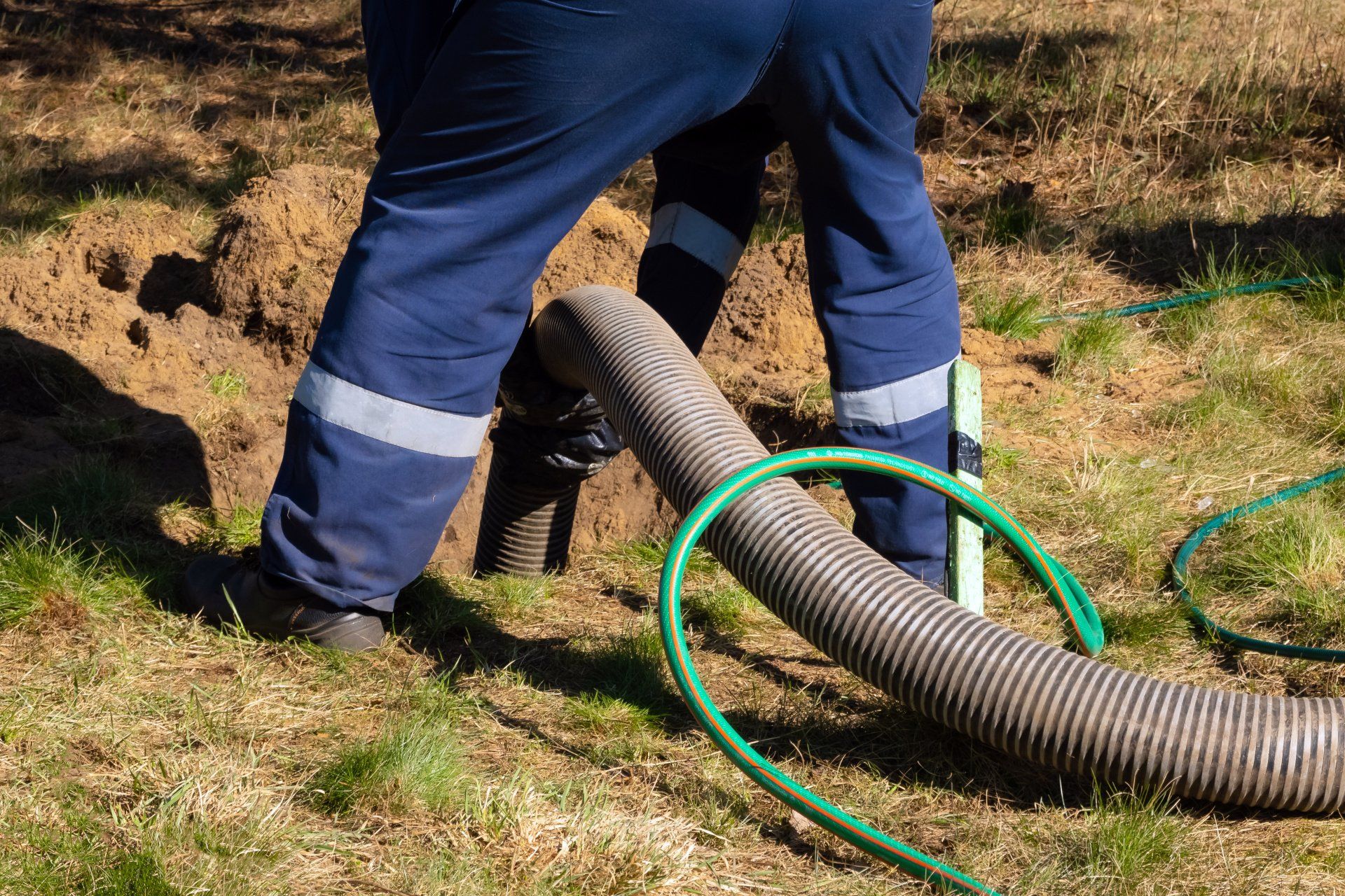 A man wearing protective gear and holding a pipe while providing sewer cleaning service outdoors.