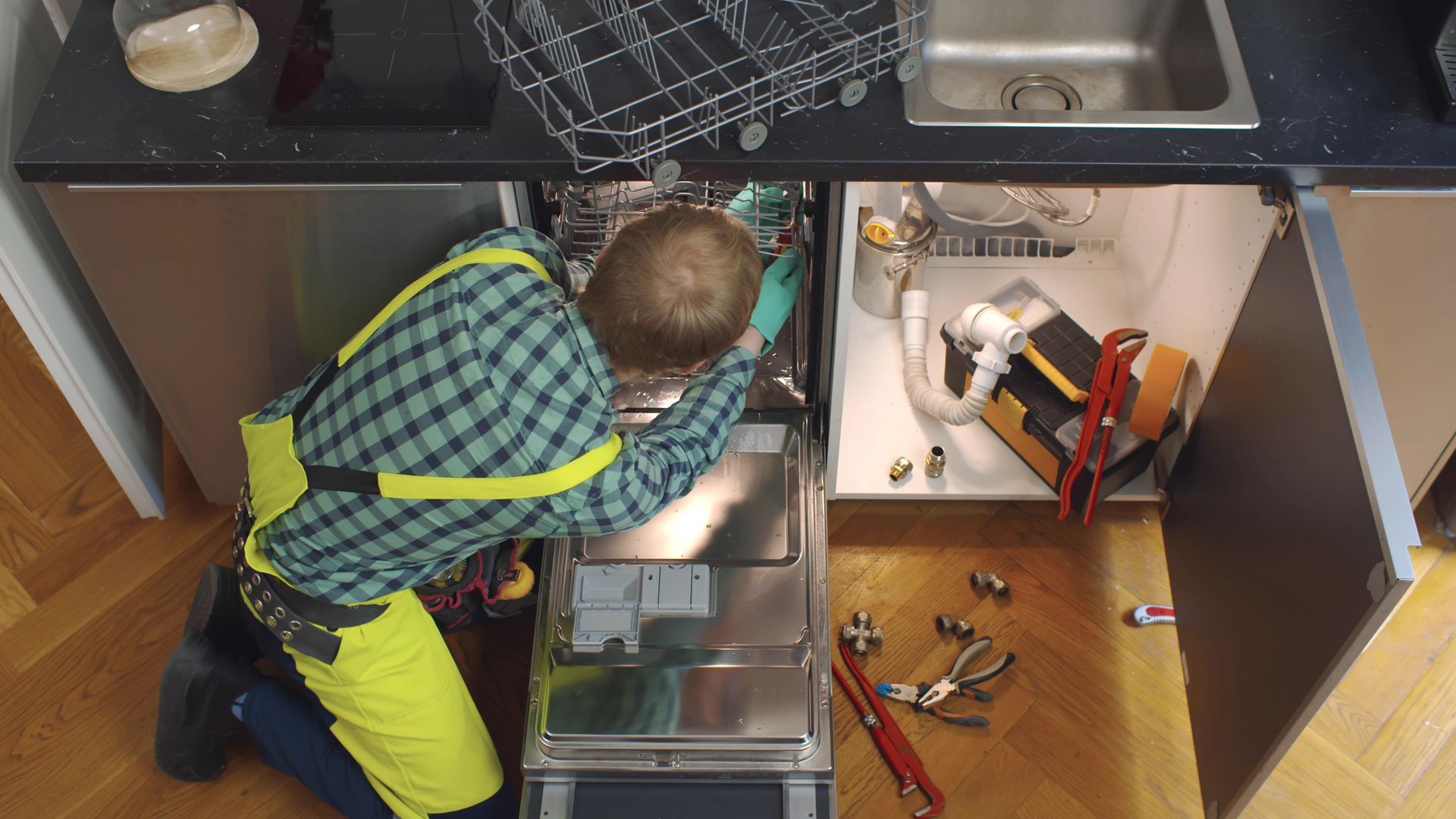 a man in a plaid shirt is working on a dishwasher