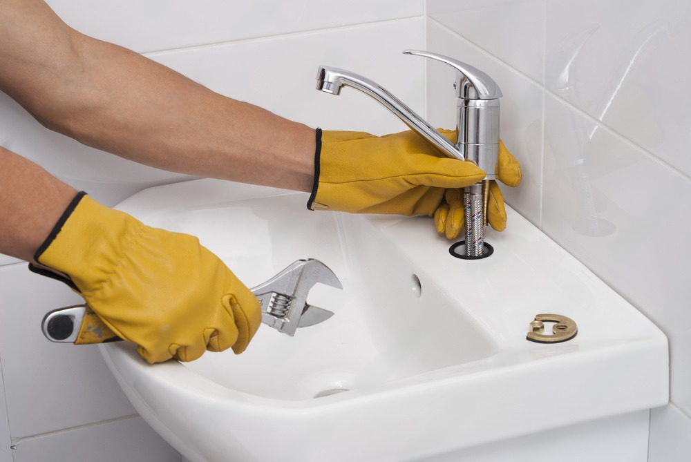 a person wearing yellow gloves is fixing a sink with a wrench