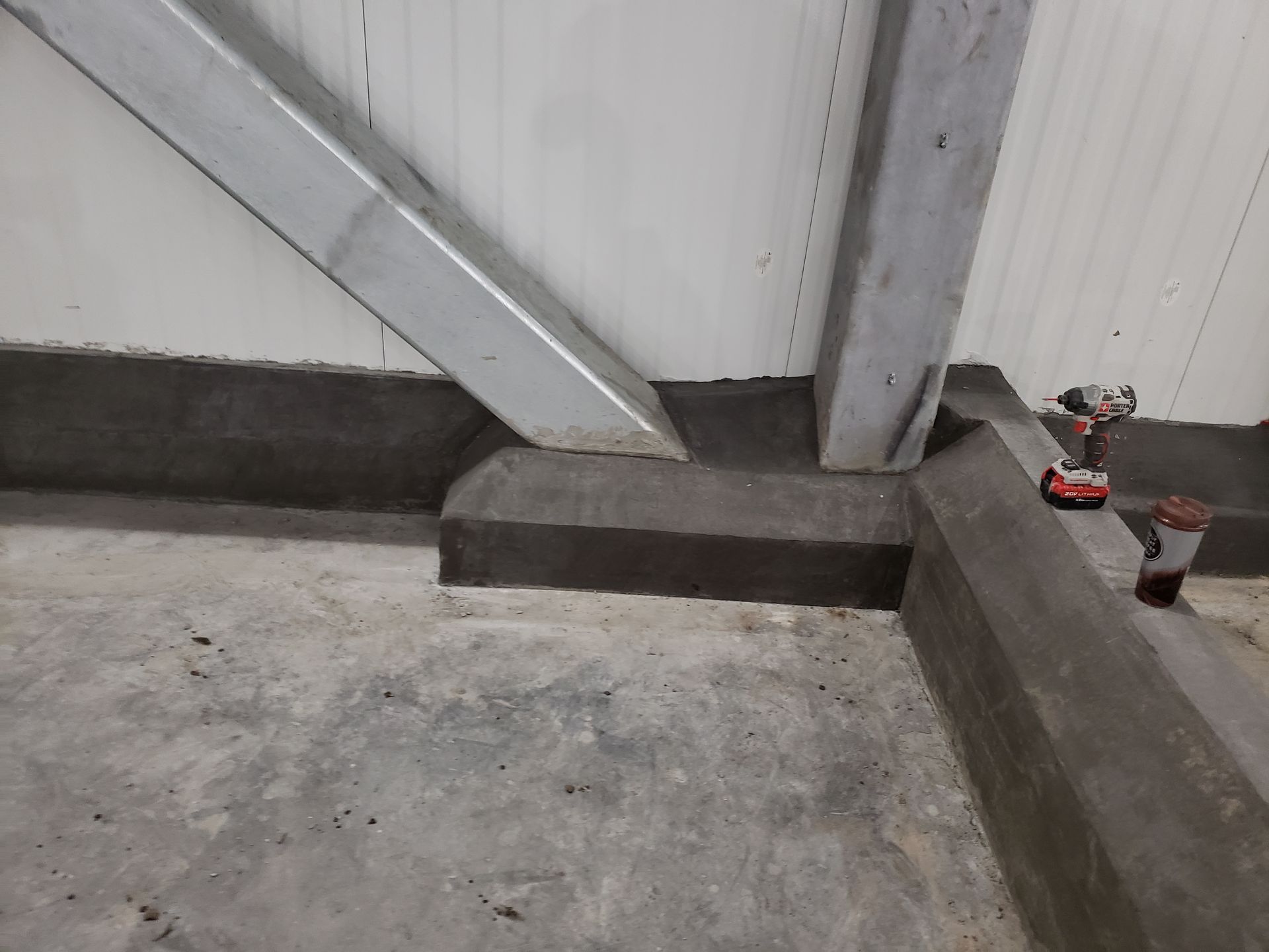 A drill is sitting on the floor next to a metal structure.