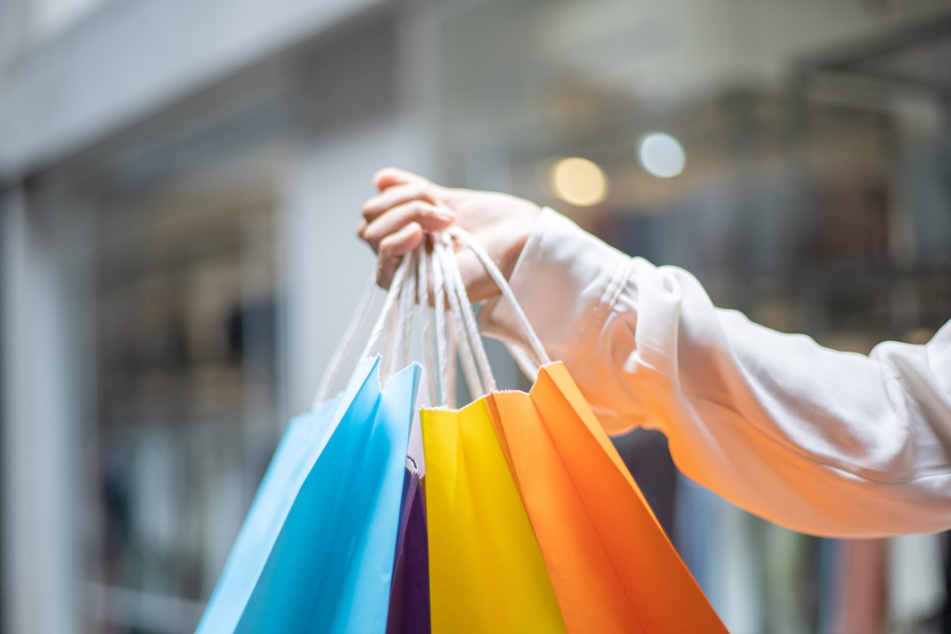 Uma mulher está segurando um monte de sacolas coloridas de compras em um shopping.