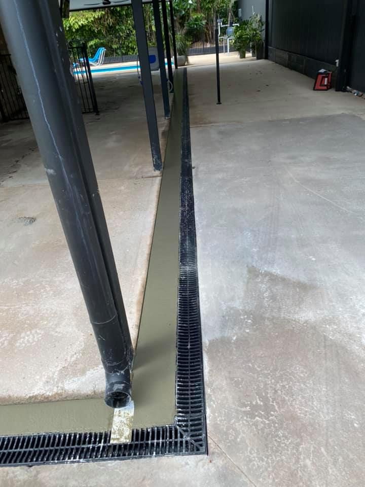 Black drain installed in concrete next to a building. Gray cement is around the drain — Dwayne Hamlyn Concreting in Woodroffe, NT