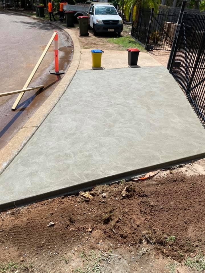 Newly poured concrete driveway with a curb, bins, and a work truck in the background — Dwayne Hamlyn Concreting in Woodroffe, NT