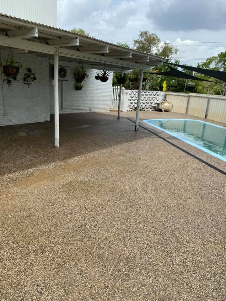 Patio area with a pool. White building, covered patio, brown concrete floor, blue-lined pool, sunny outdoors — Dwayne Hamlyn Concreting in Woodroffe, NT