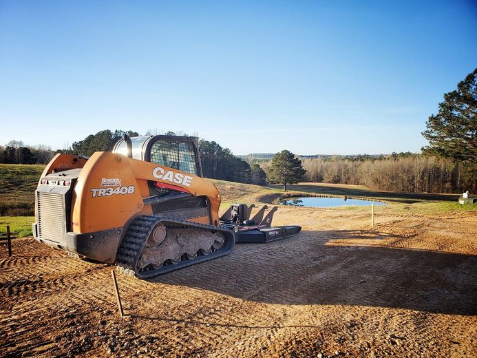 Orange Case skid steer on a gravel area, trees and pond in the background, sunny day.